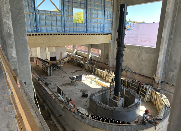 Inde i byggeriet ses en stor, rund betonstruktur under opførelse midt i et rum med rå vægge, stilladser og byggematerialer.